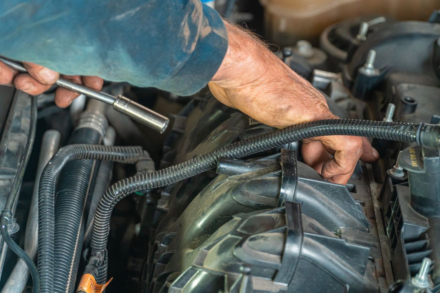 Hands with a socket wrench working across the belt and accessory area of an engine