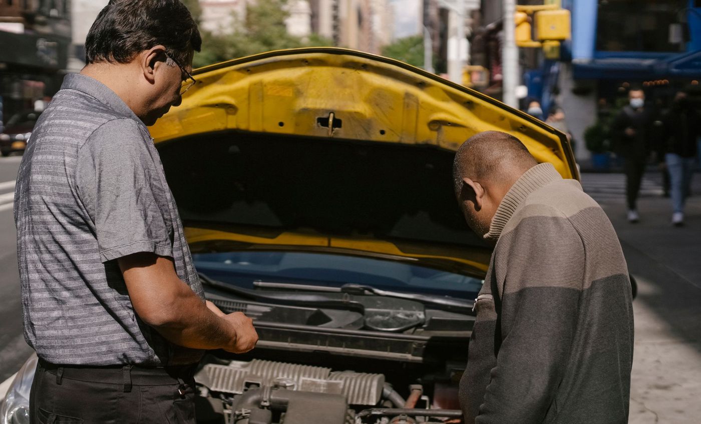 A mechanic and a driver looking over an engine bay at the roadside